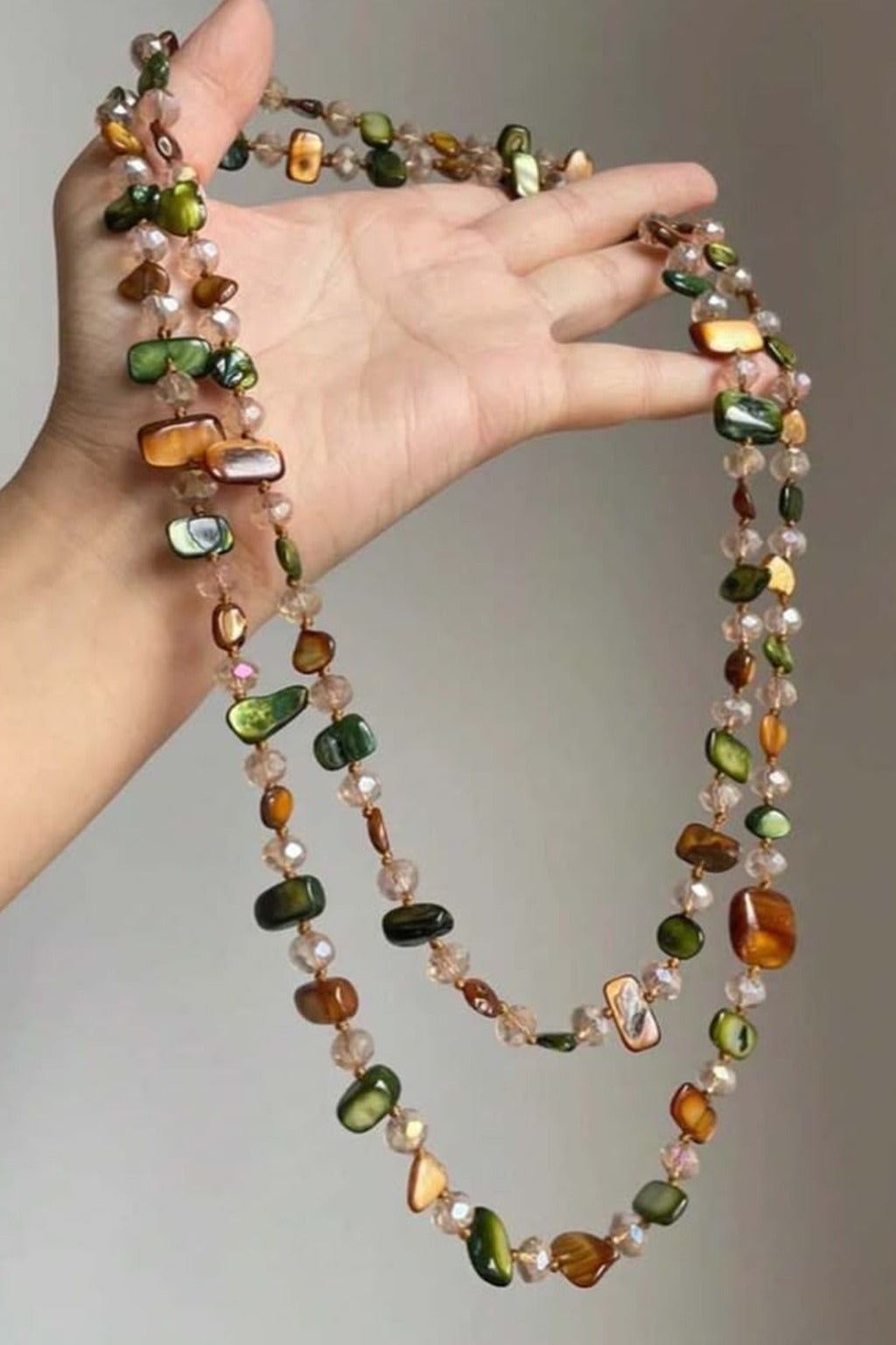 Mermaid Wrap Necklace held in hand – green and amber shell chips with crystal beads