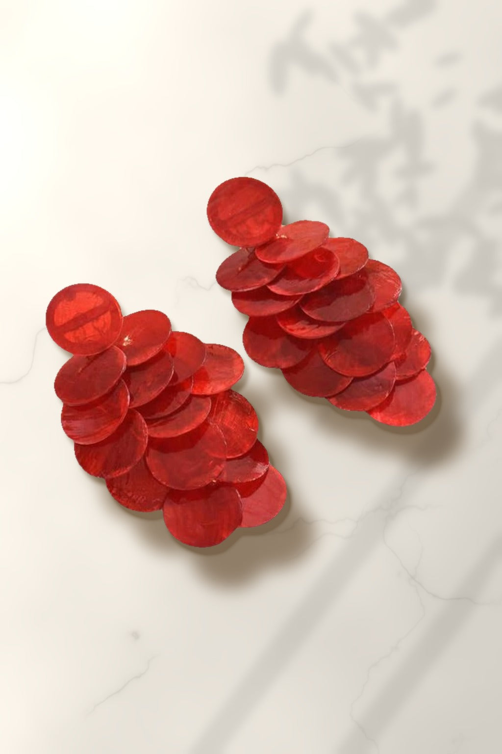 Red Shell Cascade Earrings – red capiz shell disc drop earrings on white marble in warm golden-hour sunlight